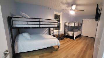 A compact room with bunk beds, a small wooden table, a white door, and a ceiling fan.