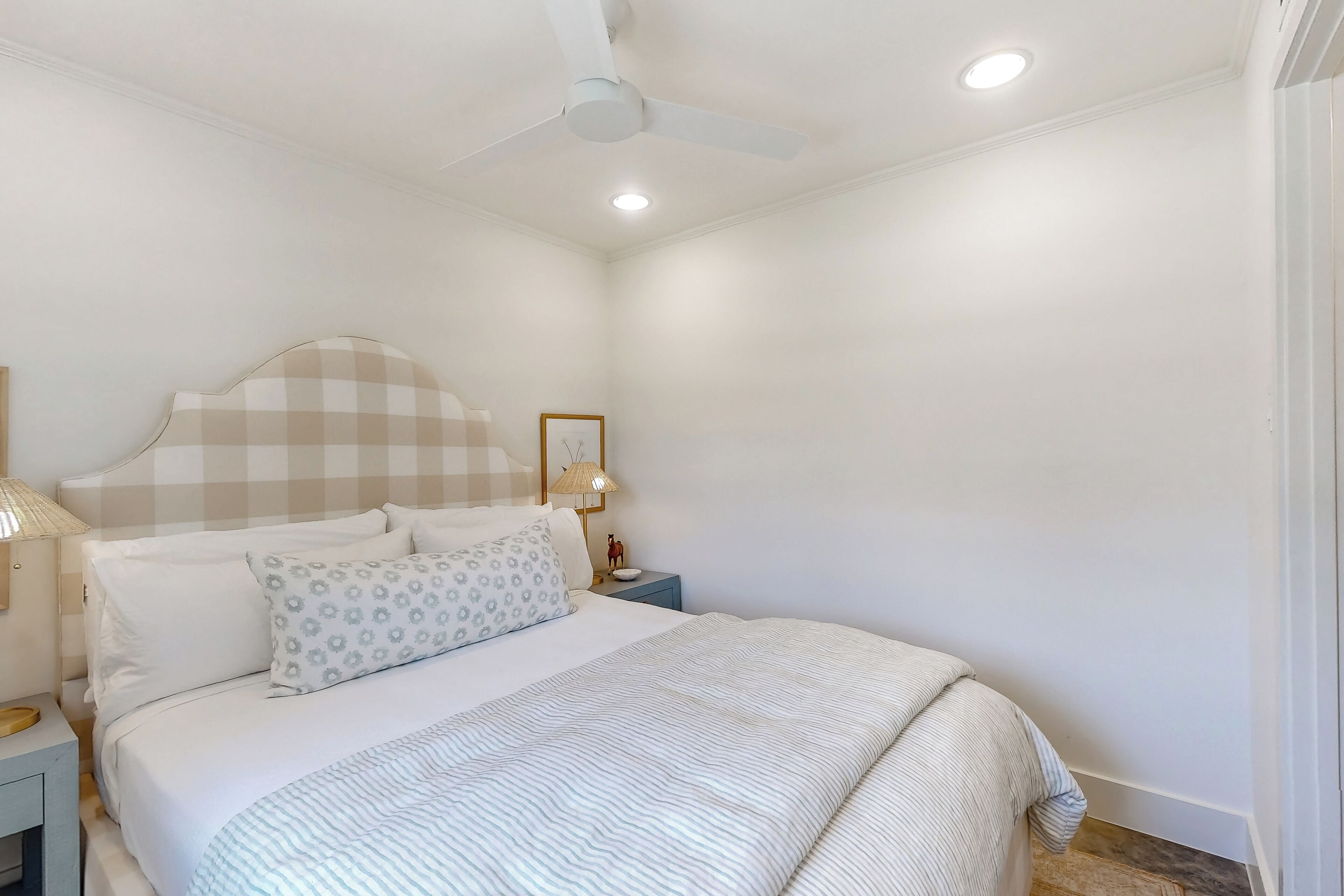 Une chambre à coucher comprenant un lit, une table de chevet, un ventilateur de plafond et une lampe fixée au mur.