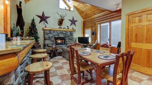 A cozy lodge interior with a stone fireplace, wooden dining table, and rustic decor. - Near Dtwn Pigeon Forge! Multi-Level Cabin w/ Pool (Pigeon Forge)