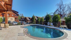 A pool area with a wooden deck, a sign indicating shallow water, and a view of cabins in the background. - Near Dtwn Pigeon Forge! Multi-Level Cabin w/ Pool (Pigeon Forge)