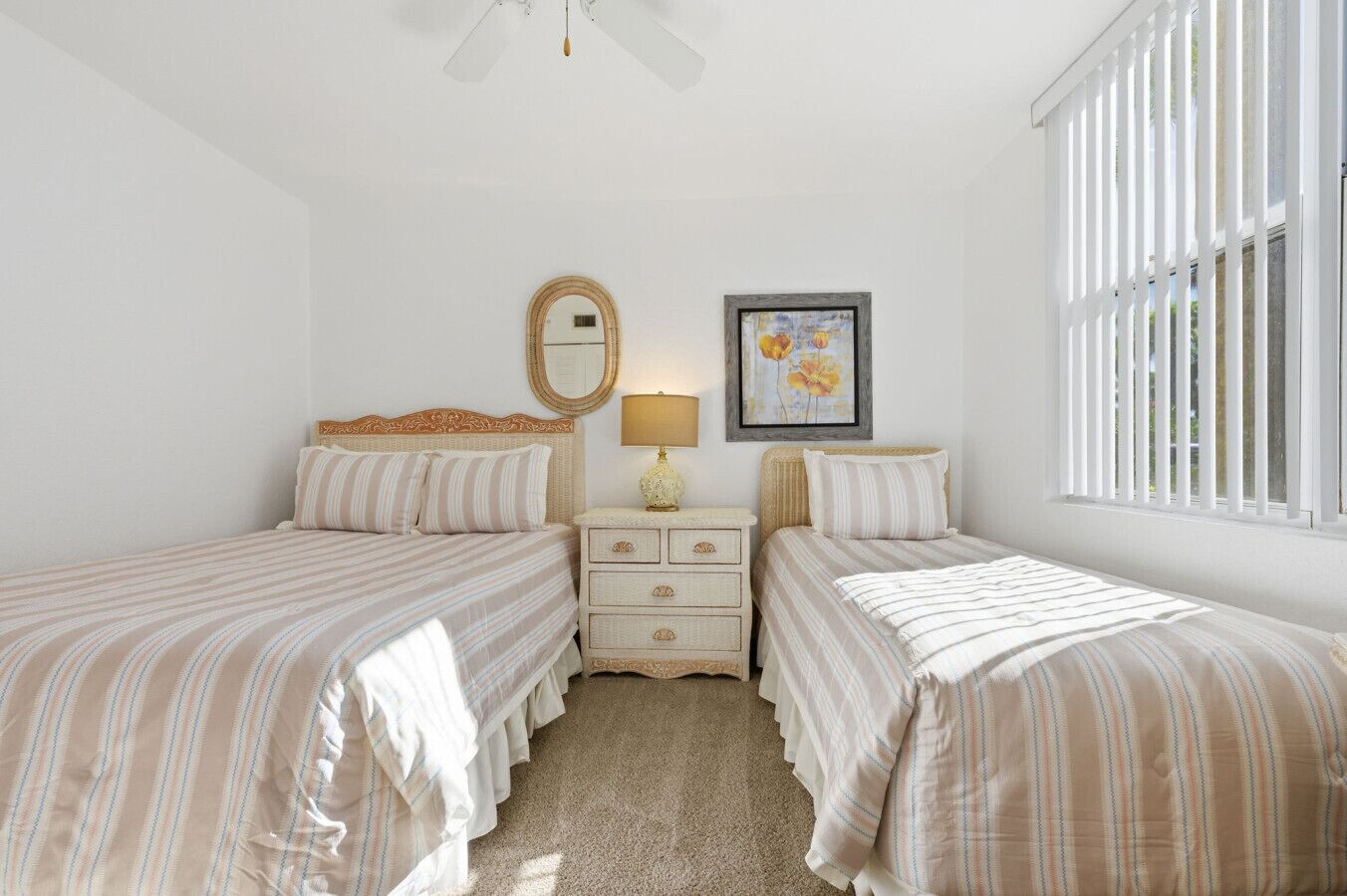 A bedroom with two beds, a dresser, a mirror, a framed picture, and a window with blinds.