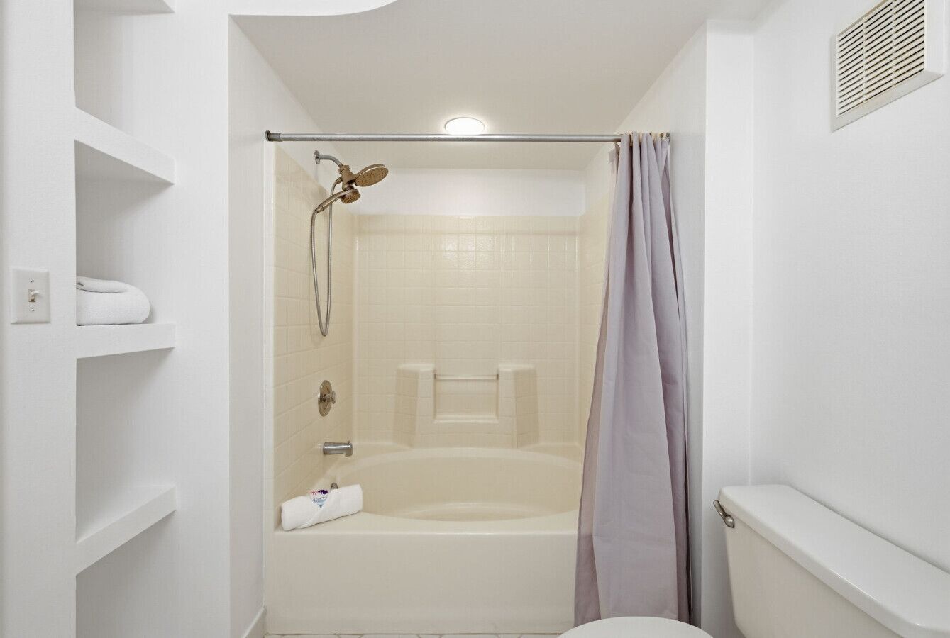 A bathroom with a bathtub, shower, toilet, and shelves.