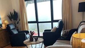 A modern living room with a large window, two black armchairs, a round coffee table, and a sofa with a throw pillow. - Loft Eira Cálm&luxury Views Sierra Nevad Parking included (Sierra nevada)