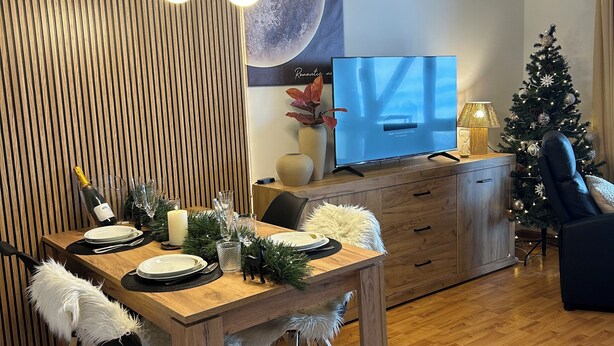 A modern living room with a wooden dining table set for four, a television, a Christmas tree, and a decorative wall panel. - Loft Eira Cálm&luxury Views Sierra Nevad Parking included (Sierra nevada)