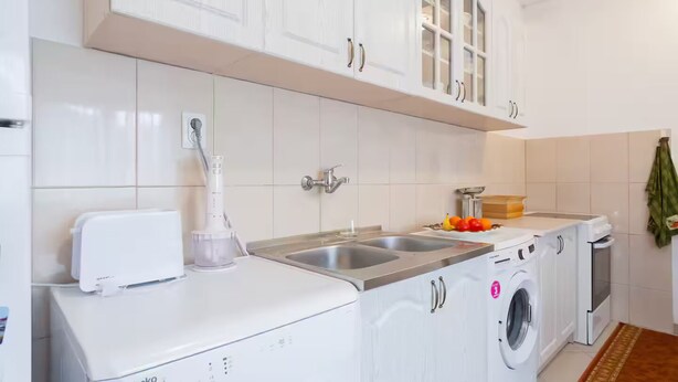 A compact kitchen with white cabinets, a built-in washing machine, and a sink. - Giant 3-bedroom house in Susanj,Bar Montenegro (Šušanj)