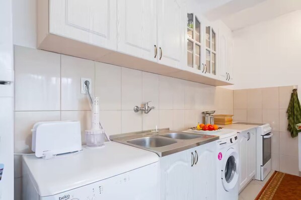 A compact kitchen with white cabinets, a built-in washing machine, and a sink.