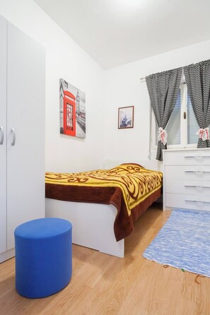 A bedroom with a bed, a wardrobe, a blue stool, a window with patterned curtains, and two wall-mounted pictures. - Giant 3-bedroom house in Susanj,Bar Montenegro (Šušanj)