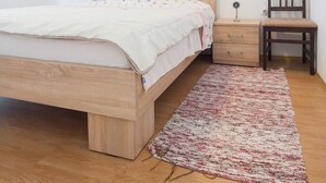 Une chambre à coucher avec un lit en bois, une table de chevet, une chaise, une petite table et un tableau accroché au mur.
