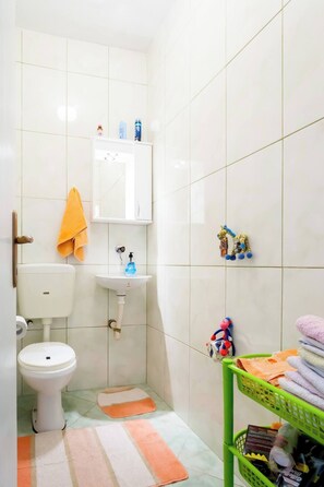 A small bathroom with a toilet, sink, and a green basket with towels. - Giant 3-bedroom house in Susanj,Bar Montenegro (Šušanj)