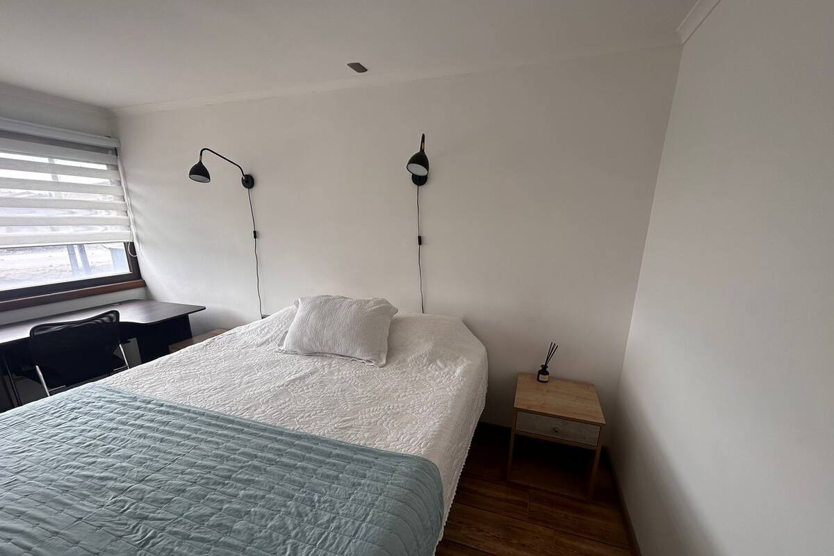 A bedroom with a bed, a desk, and two wall-mounted lamps.