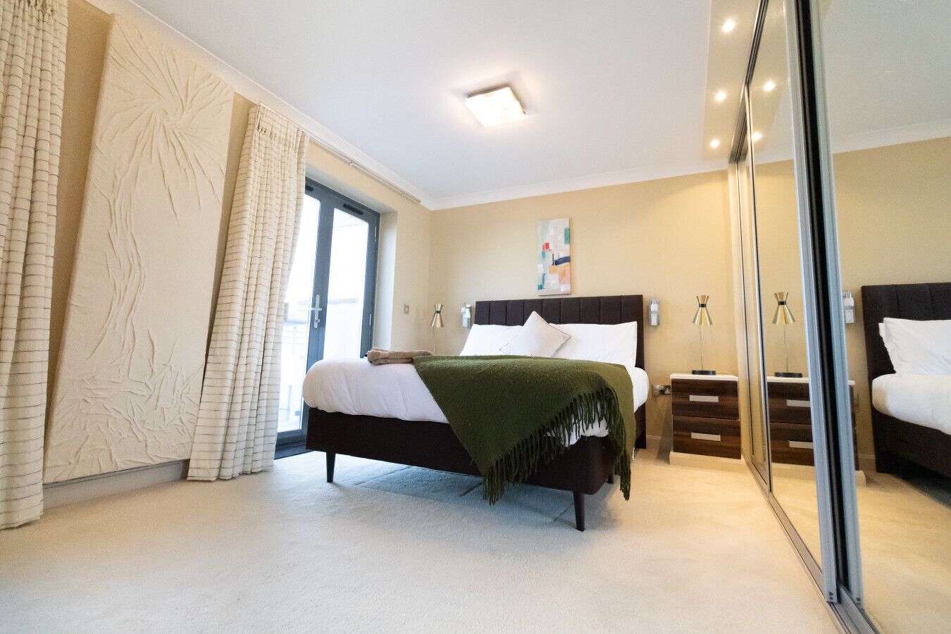 A modern bedroom with a large bed, a wardrobe, and a sliding glass door to a balcony.