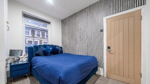 Quarto com uma cama grande, mesa de cabeceira, janela e porta.