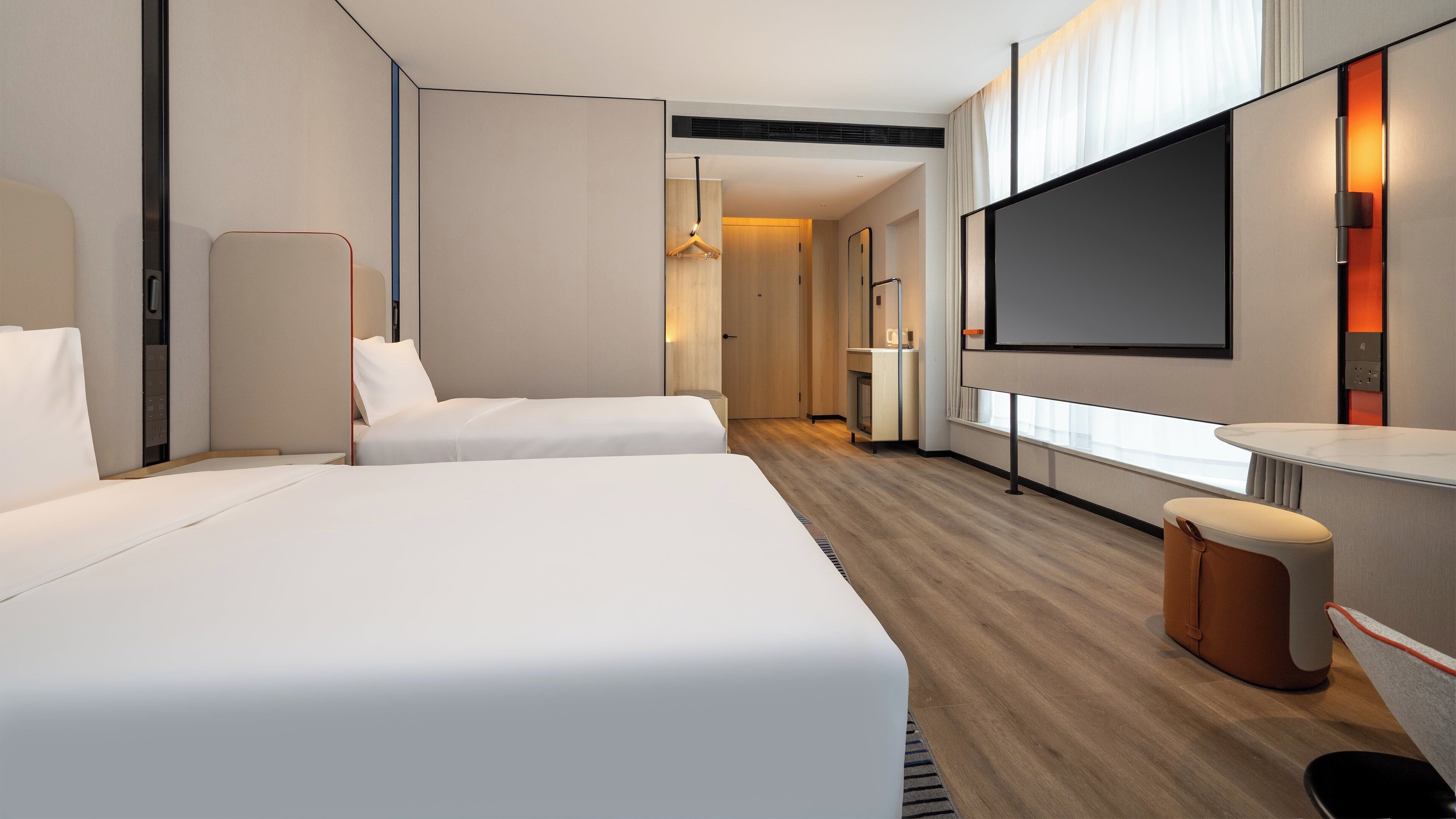 A modern hotel room with two beds, a large flat-screen TV, a desk, and a seating area.