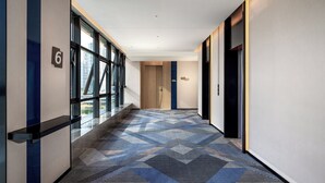 A modern hotel corridor with a geometric patterned carpet, large windows, and a wooden door. - Holiday Inn Express Chengdu Phoenix Mountain By Ihg (Chengdu)
