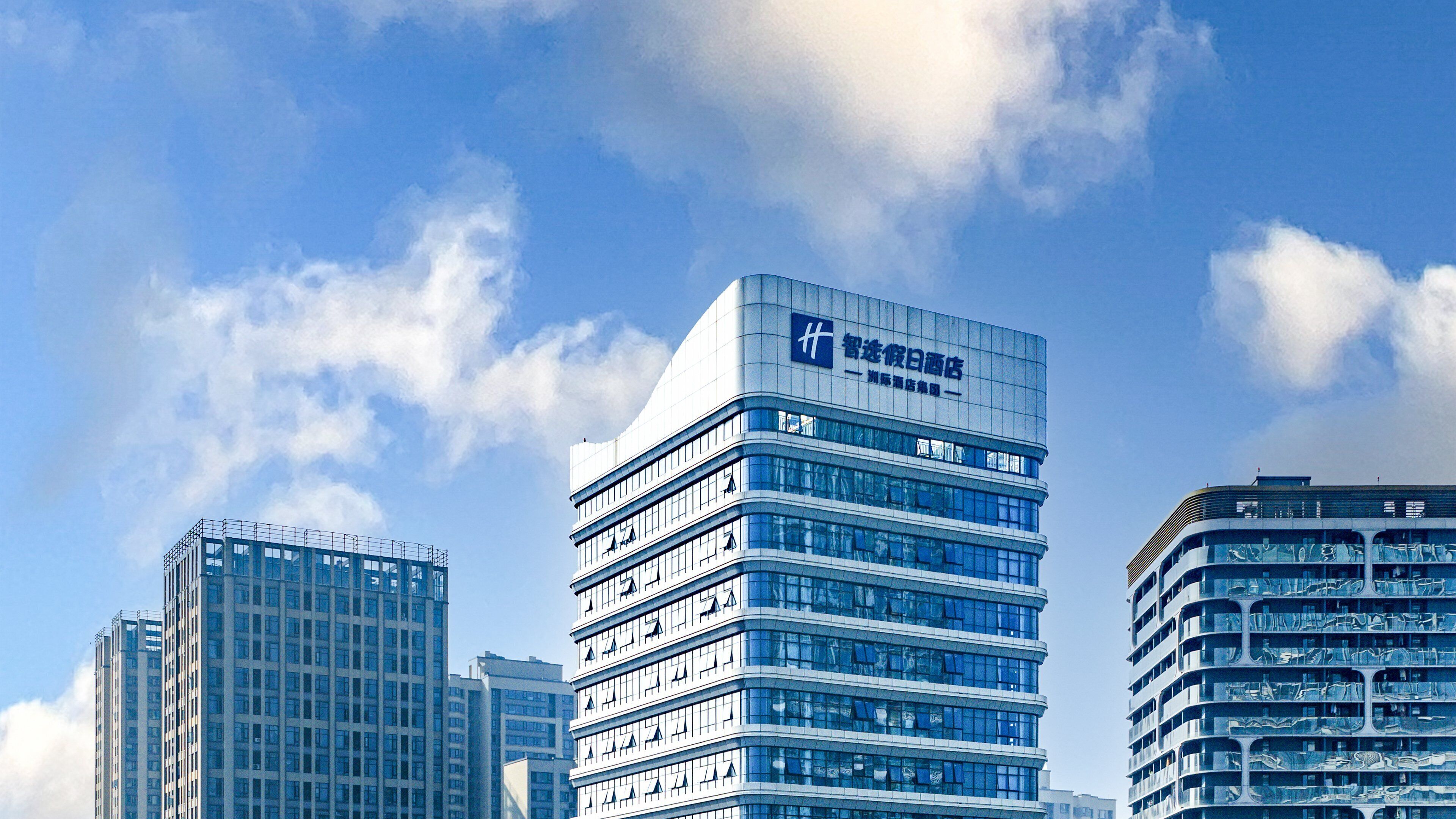 A modern hotel with a glass facade, multiple floors, and a prominent signage.
