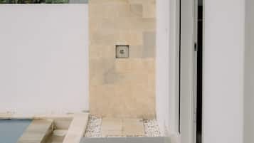A modern outdoor shower area with a stone wall, a pool, and a pathway leading to a door.