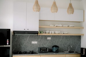 A modern kitchen with a gas stove, a toaster, a coffee maker, and a sink. There are wicker pendant lights and a marble backsplash. - Casa Verona Villa Lovina Bali (Buleleng)