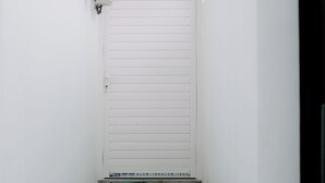A white door with a small step leading up to it, a security camera above, and a green hose on the ground. - Casa Verona Villa Lovina Bali (Buleleng)