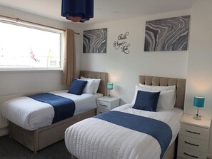 Une chambre d’hôtel avec deux lits, chacun recouvert d’une couvre-lit bleue et blanche, une table de chevet avec une lampe et une fenêtre avec des rideaux.