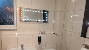 Et badeværelse med en hvid vask, toilet og et spejl med lys.