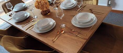 A dining table set with white plates, gold cutlery, and wine glasses, surrounded by mustard-colored chairs.