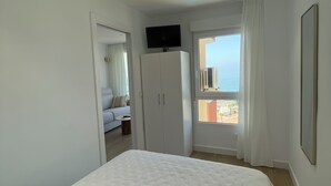 Ein Schlafzimmer mit einem großen Bett, einem an einer Kommode befestigten Fernseher und einem Fenster mit Blick nach draußen.