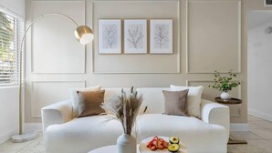 Een moderne woonkamer met een witte bank, een vloerlamp en drie ingelijste botanische afbeeldingen aan de muur.