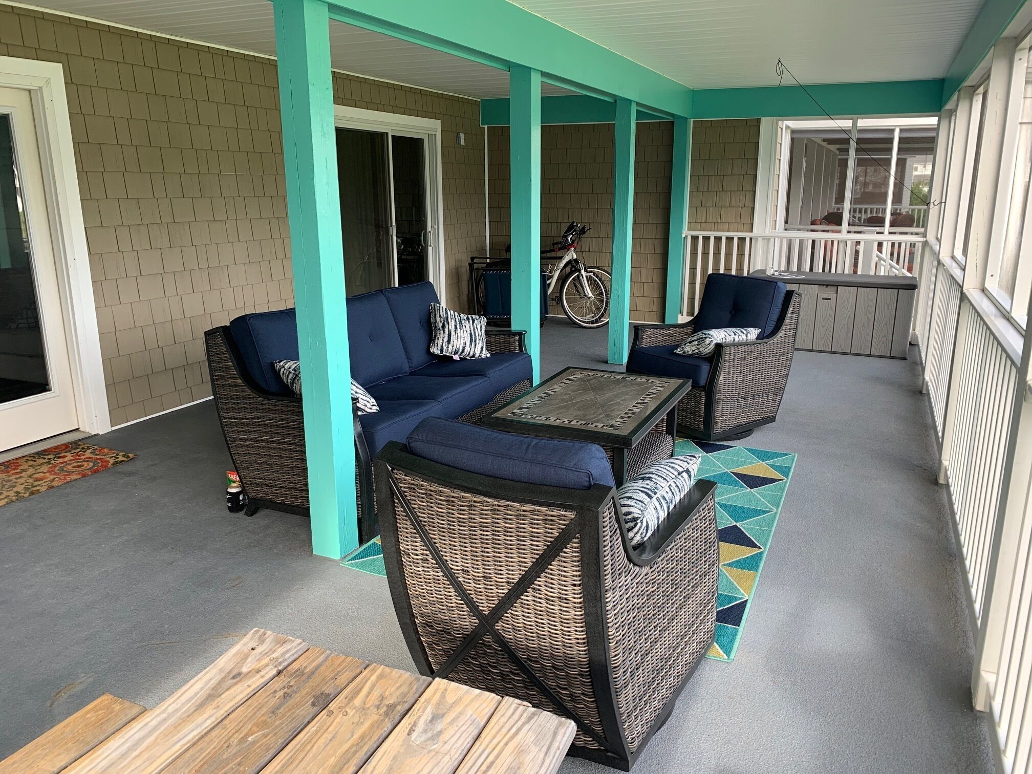 A covered patio area with wicker furniture, a table, and a bicycle in the background.
