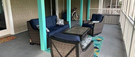 A covered patio area with wicker furniture, a table, and a bicycle in the background.