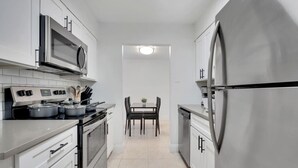 A narrow kitchen with stainless steel appliances, white cabinets, and a dining area with a table and chairs. - Bayshore Bliss | King Suite + Pool & Gym (Tampa)