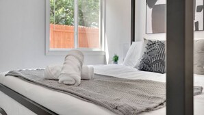 A modern bedroom with a large window, a neatly made bed, and a small plant on the nightstand. - Bayshore Bliss | King Suite + Pool & Gym (Tampa)