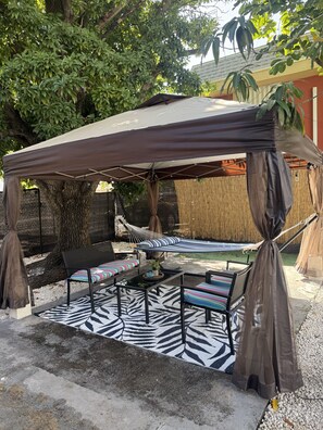 A covered outdoor seating area with a hammock, a zebra-patterned rug, and a table with chairs. - 5 Mins to Brickell & Downtown - 2BR + Free Parking, Private Patio, Pets Ok (Miami)