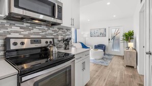 Una cocina moderna con electrodomésticos de acero inoxidable, una tetera en la hornilla y una silla azul al fondo.