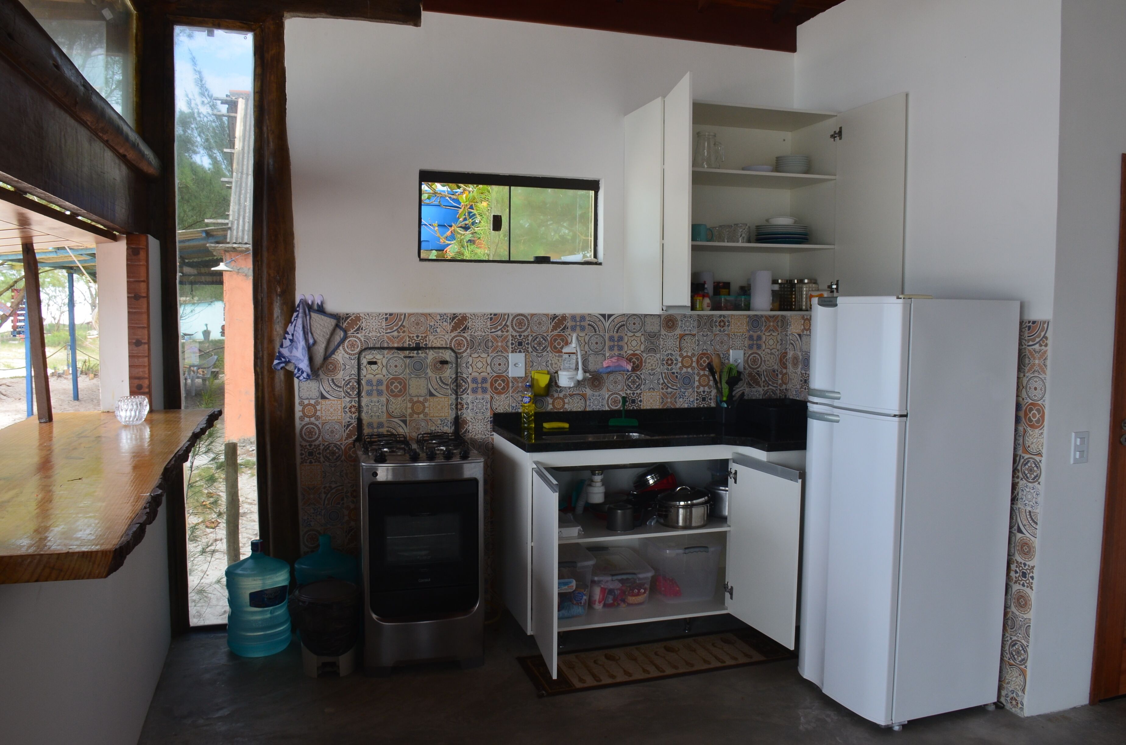 Eine kleine Küche mit Kühlschrank, Herd und Fenster mit Blick auf einen Garten.