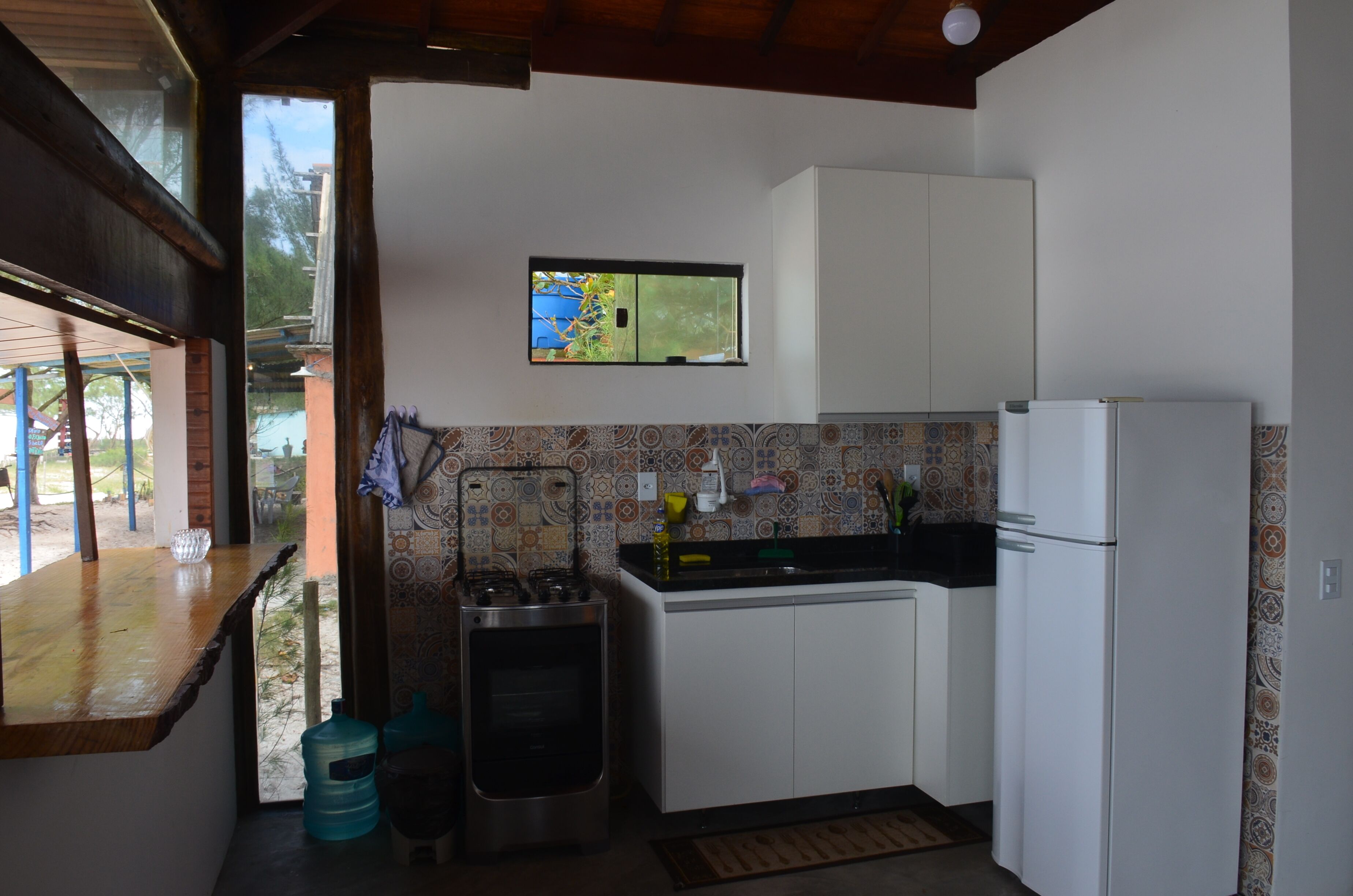 A compact kitchen with a gas stove, a sink, and a refrigerator. A window with a view of the outdoors is visible above the sink.