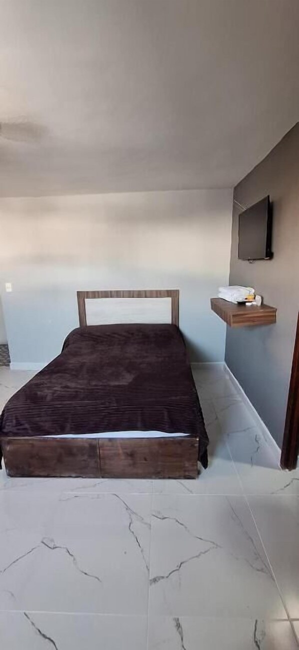 A bedroom with a bed, a flat-screen TV mounted on the wall, and a small wooden shelf with items on it. - Casa Hidalgo Hotel (Torreon)