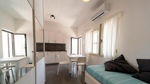 Ein kleines Zimmer mit Bett, Schreibtisch, Stuhl und einer Küchenzeile.