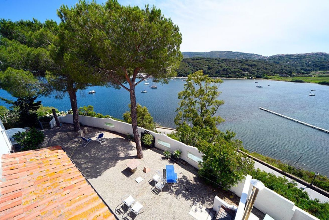 A terrace with outdoor seating, a tree, and a view of a lake with boats.