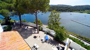 Eine Terrasse mit Sitzgelegenheiten im Freien, ein Baum und Blick auf einen See mit Booten.