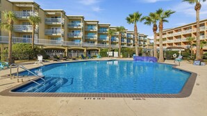 Ett hotell med en swimmingpool omgiven av palmer och en flervåningsbyggnad med balkonger.