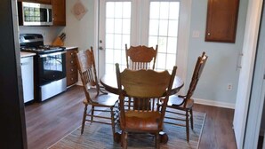 Un comedor con mesa y sillas de madera, una cocina con estufa y microondas, y una puerta con paneles de vidrio.