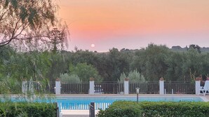 A swimming pool with a fence, surrounded by greenery and a sunset in the background. - Borgo Levante Farmhouse/Rose Room (Sicilia)