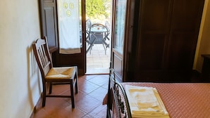 A room with a bed, a wooden chair, a table with chairs outside, and a door with curtains. - Borgo Levante Farmhouse/Rose Room (Sicilia)
