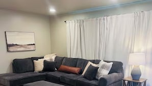 A living room with a sectional sofa, an ottoman, a rug, a lamp, and a painting on the wall. - Cozy 2-bedroom house in Enid (Enid)
