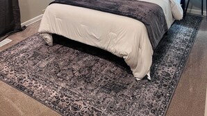 A bedroom with a large bed, a headboard, a nightstand, a lamp, a window with curtains, and a painting on the wall. - Cozy 2-bedroom house in Enid (Enid)