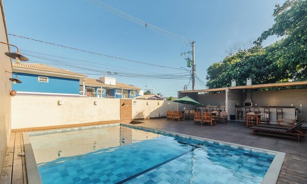 Una piscina con cubierta de madera, mobiliario exterior y vistas a edificios cercanos.