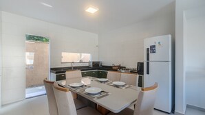 A modern kitchen with a dining table set for four, a refrigerator, and a microwave. - House in Condo w/ Pool and Barbecue Grill Bme0001 (Porto Seguro)