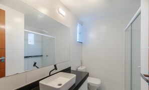 A modern bathroom with a large mirror, a white sink, a toilet, and a glass shower enclosure. - House in Condo w/ Pool and Barbecue Grill Bme0001 (Porto Seguro)
