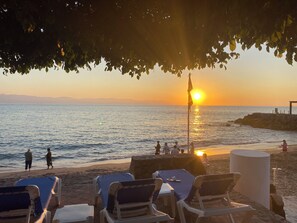 A beach with sun loungers and a table under a tree, overlooking the sea and a sunset. - Suite Villa 1 Bedroom All-Inclusive Marina Puerto Vallarta (Puerto Vallarta)