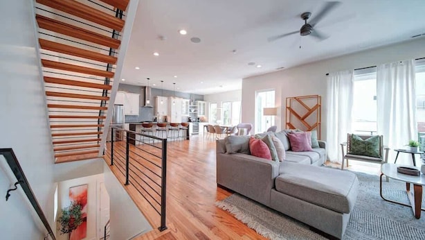 Un salón amplio con una escalera, un sofá gris y un comedor.